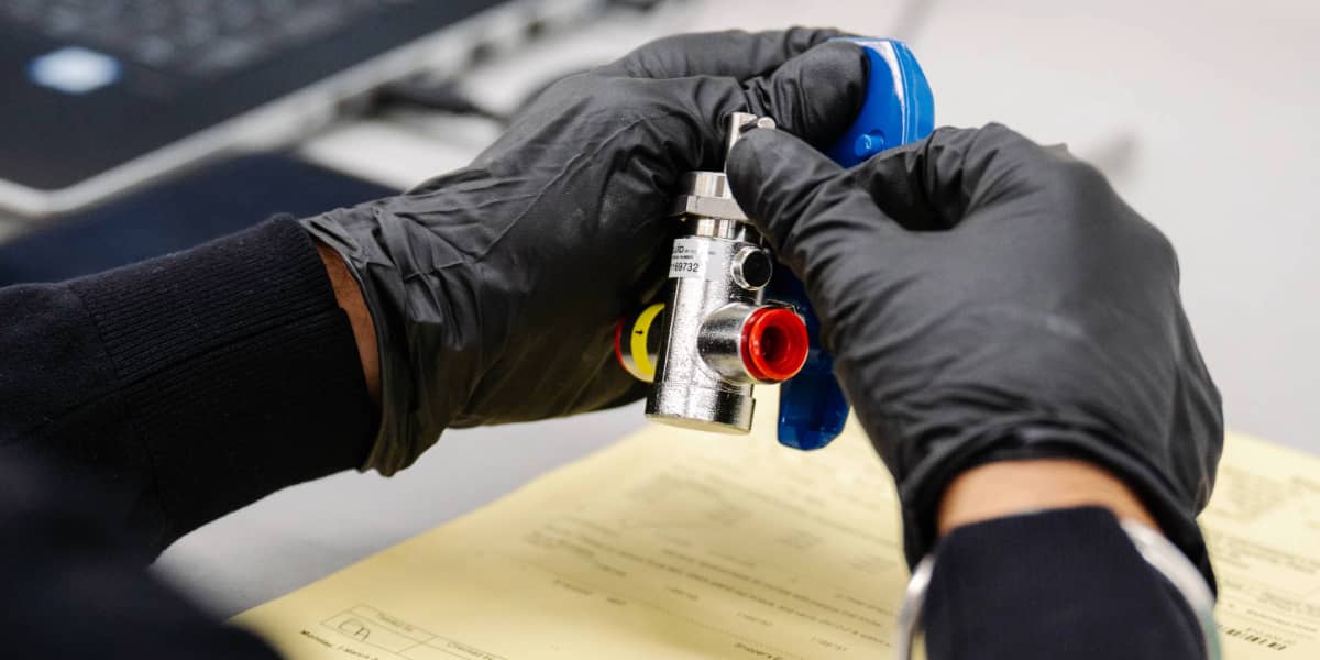  Close-up of gloved hands holding a metallic pump head device with red, yellow, and blue components