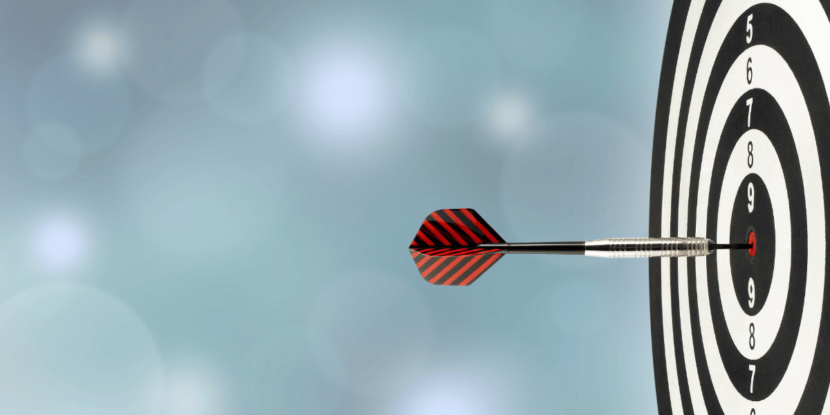 Dart hitting the bullseye on a circular dartboard with a blurred light blue background