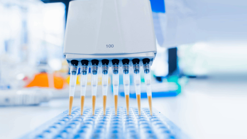 A close-up of a laboratory pipette with eight tips dispensing yellow liquid into a blue microwell plate