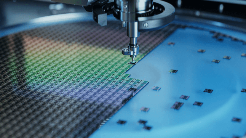 Close-up of a semiconductor wafer being processed by an automated machine, with several individual chips on a blue surface