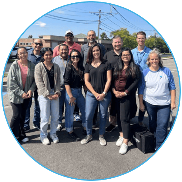 A group of twelve people posing outdoors on a sunny day.
