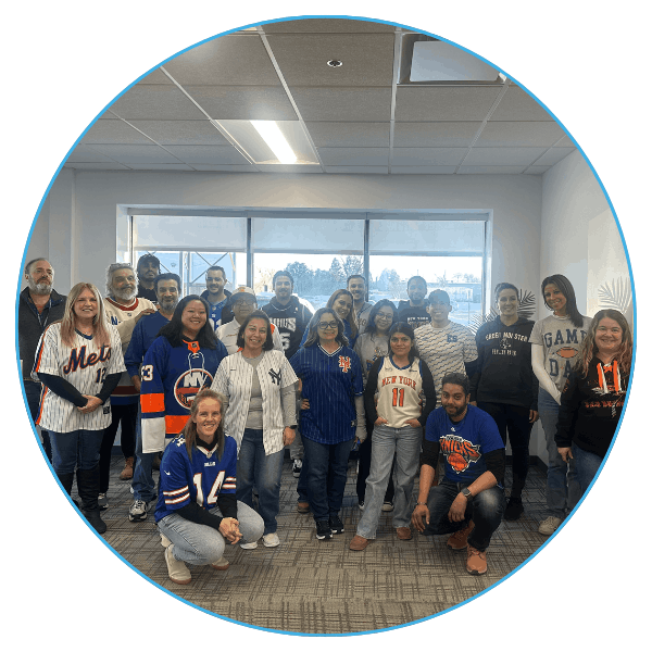 A group people, wearing various sports jerseys, stands smiling in a well-lit office room.