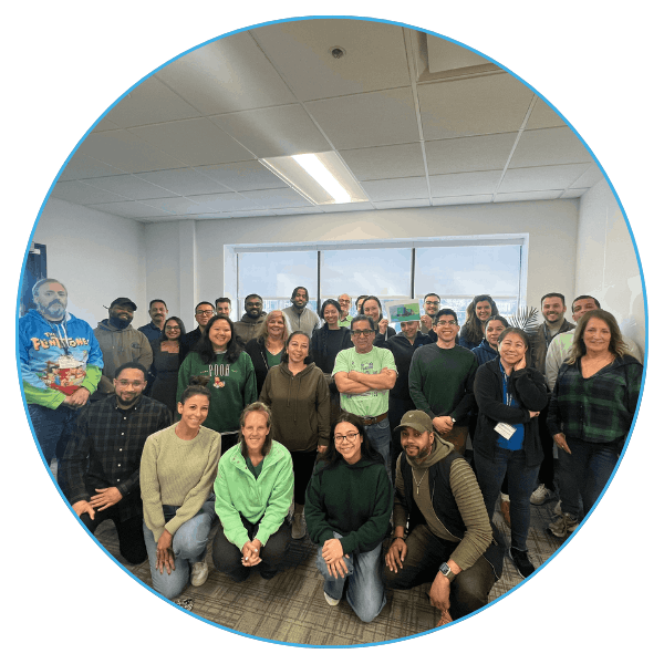 A diverse group of smiling adults in casual clothes poses in an office with a large window.