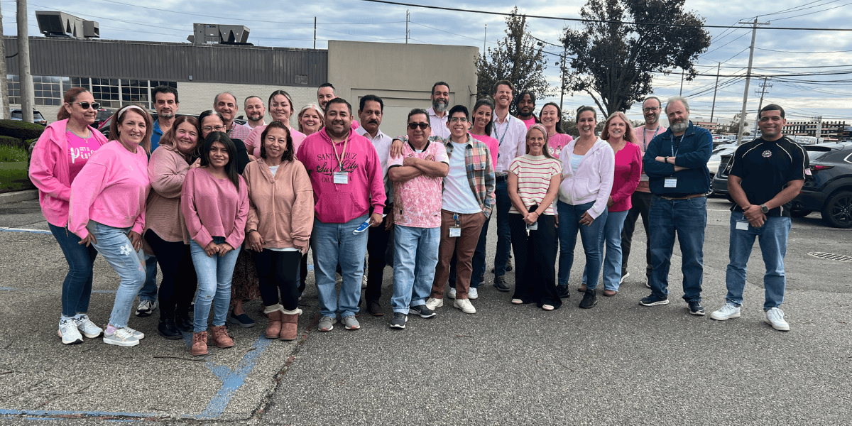 A group of team members wearing pink clothing posing in a parking lot.